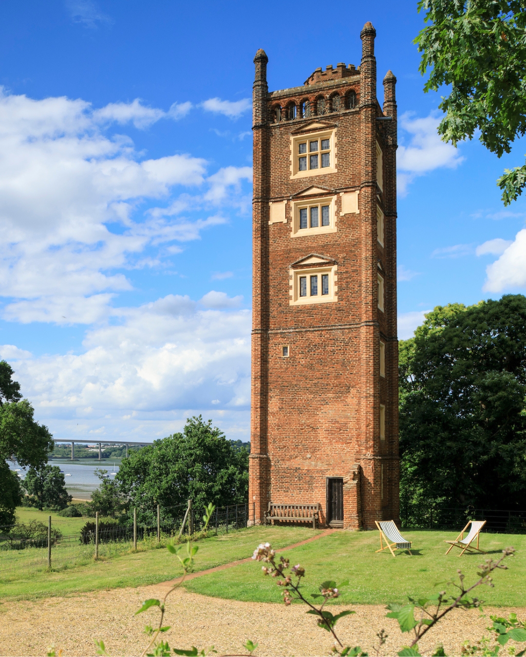 A tall brick tower stands next to a river, surrounded by trees