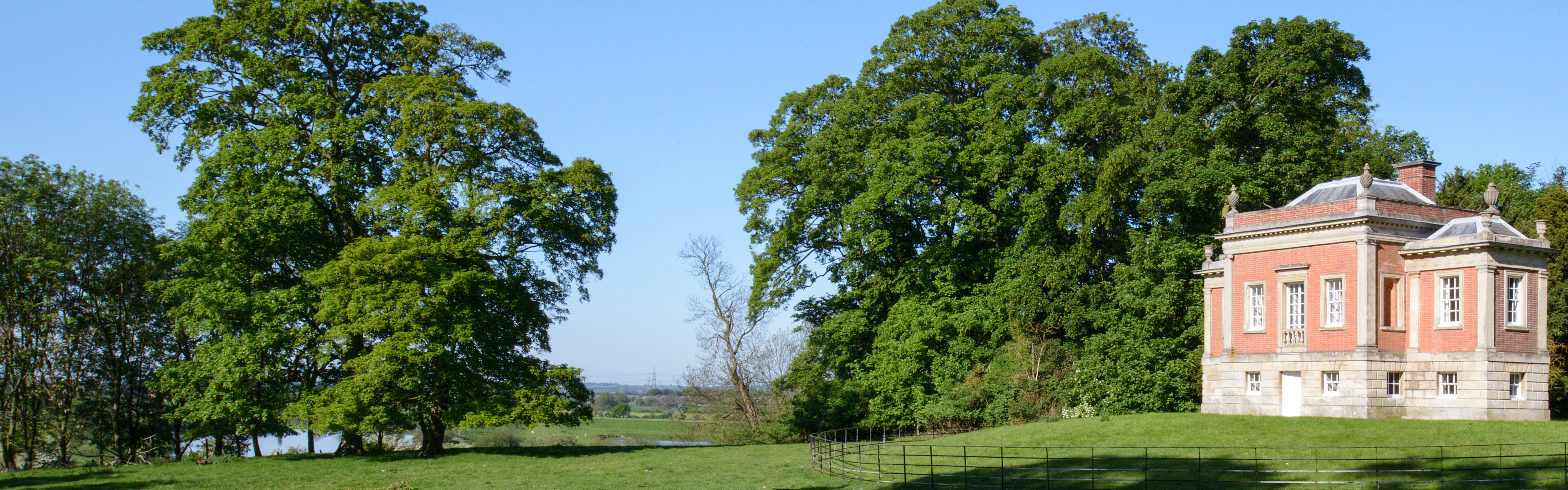 Tudor timber building stands next to a row of trees overlooking rolling countryside